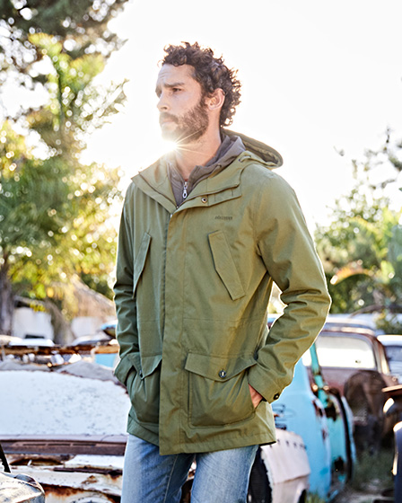 An image of a man wearing an Ayacucho jacket, stood in front of some old cars