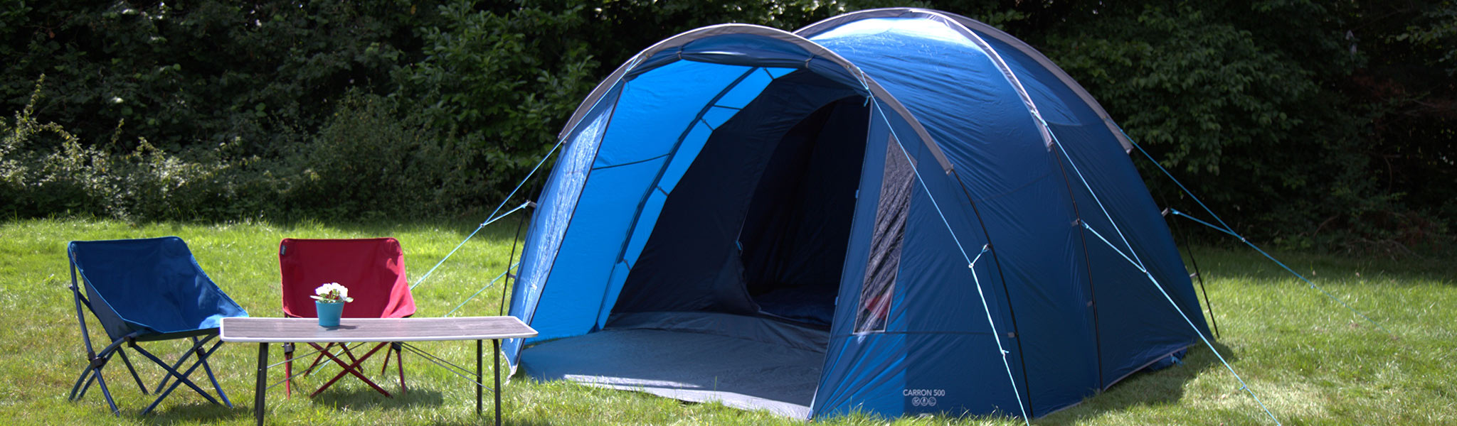 A Vango Family tent pitched in a field, with a Vango table and chairs next to the entrance 