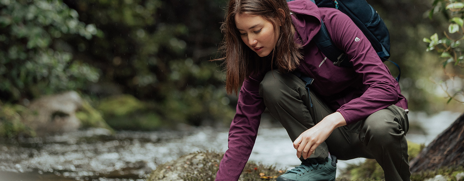 A woman gathering water from a lake in her Craghoppers clothing