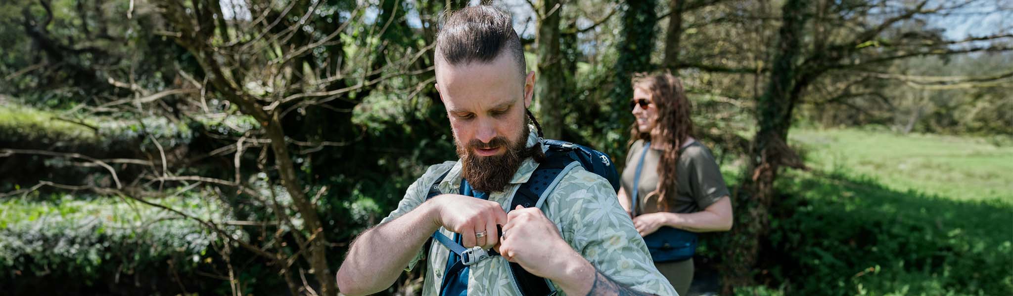 A man in a summer shirt is fastening his rucksack outdoors