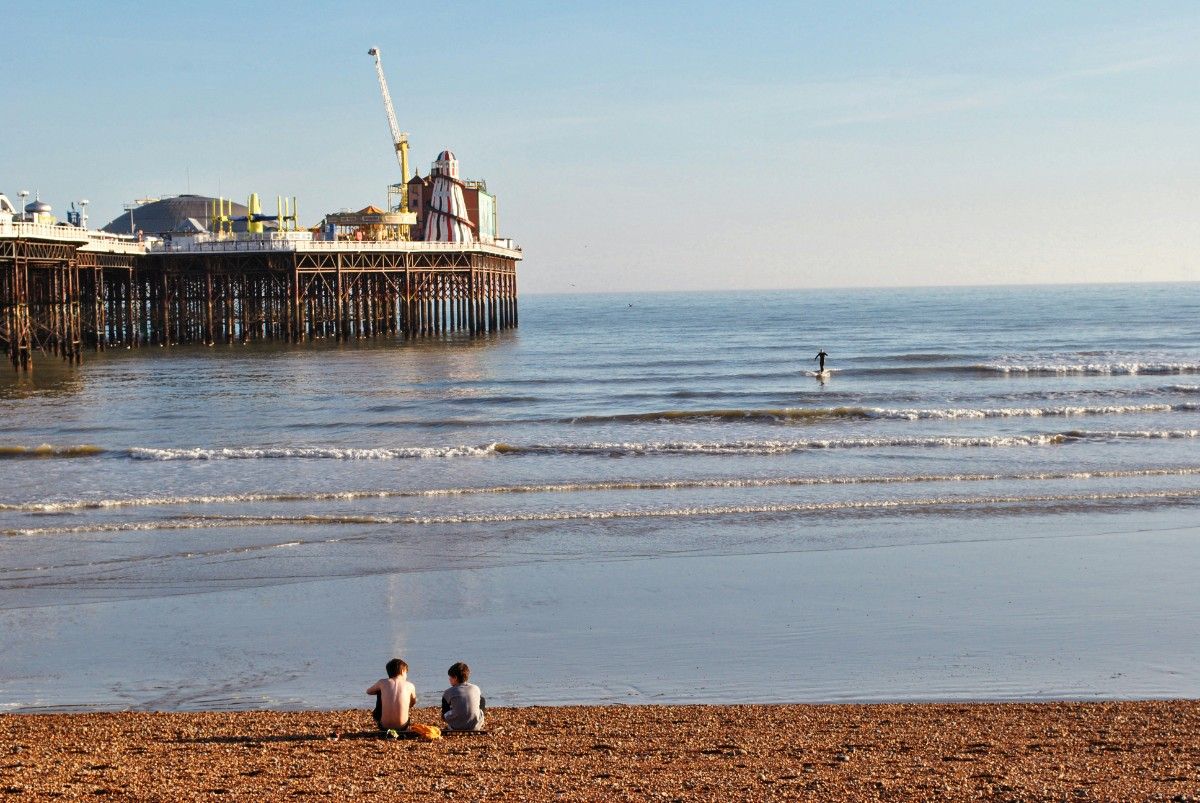 Two children sat on Brighton Beach next to the pier 