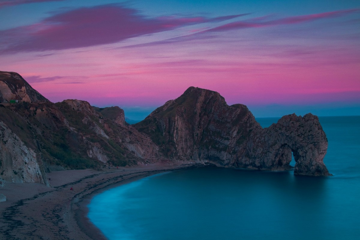 Durdle Door Beach at sunset, the sky appears purple and pink 