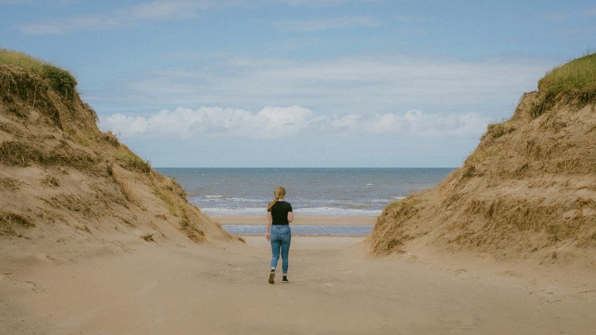 A woman stood between two dunes looking at the sea on Formby Beach