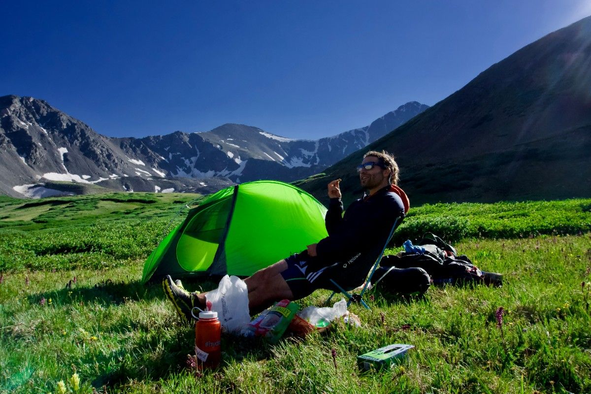 A person backpacking in the mountains, with their tent set up 