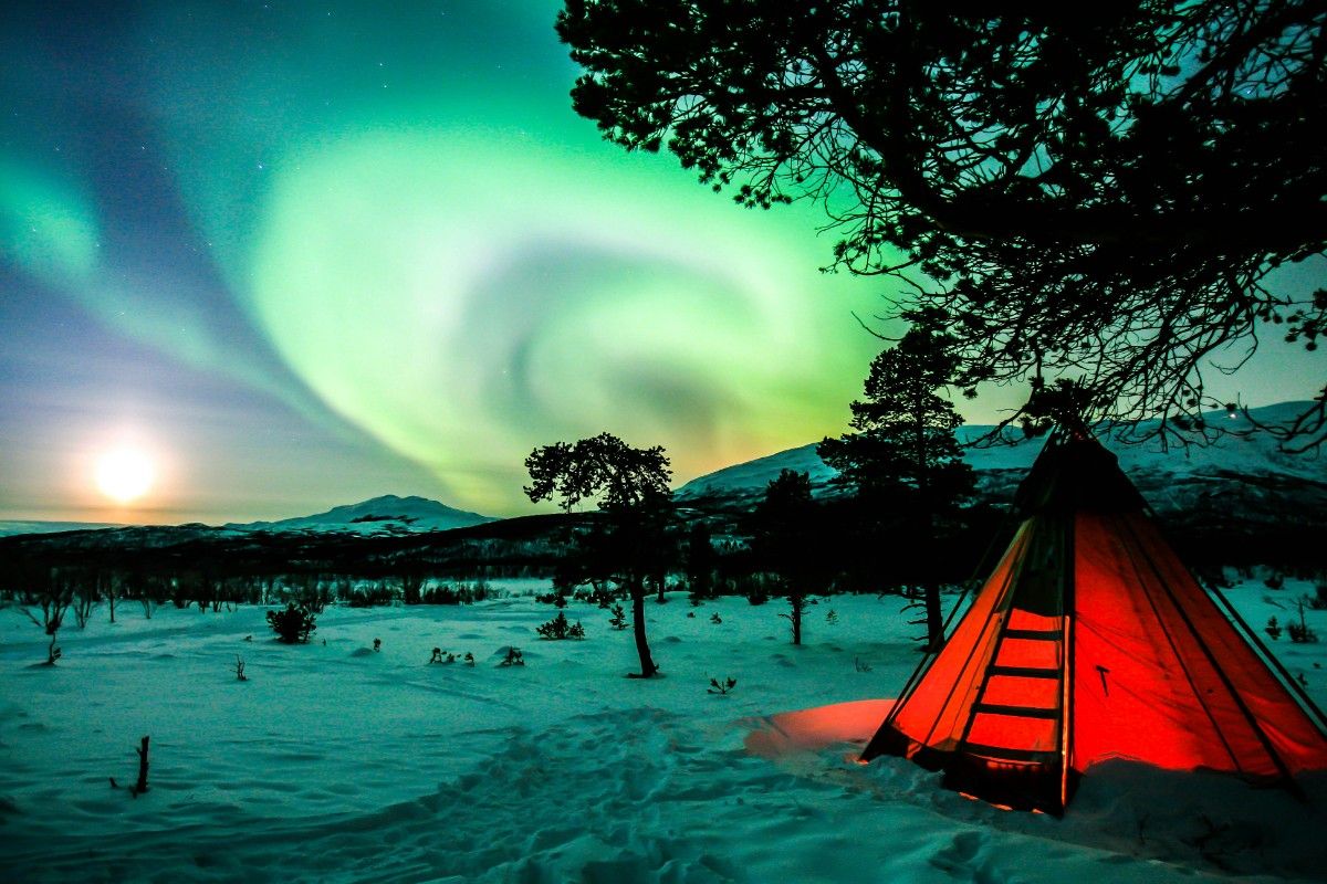 A red tent in the snow with the northern lights above 