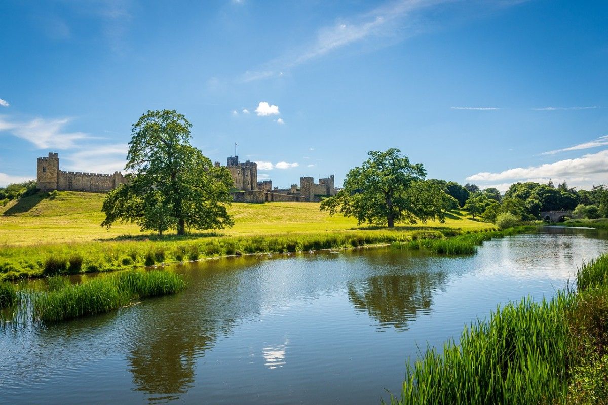 A body of water with Alnwick Castle in the distance 