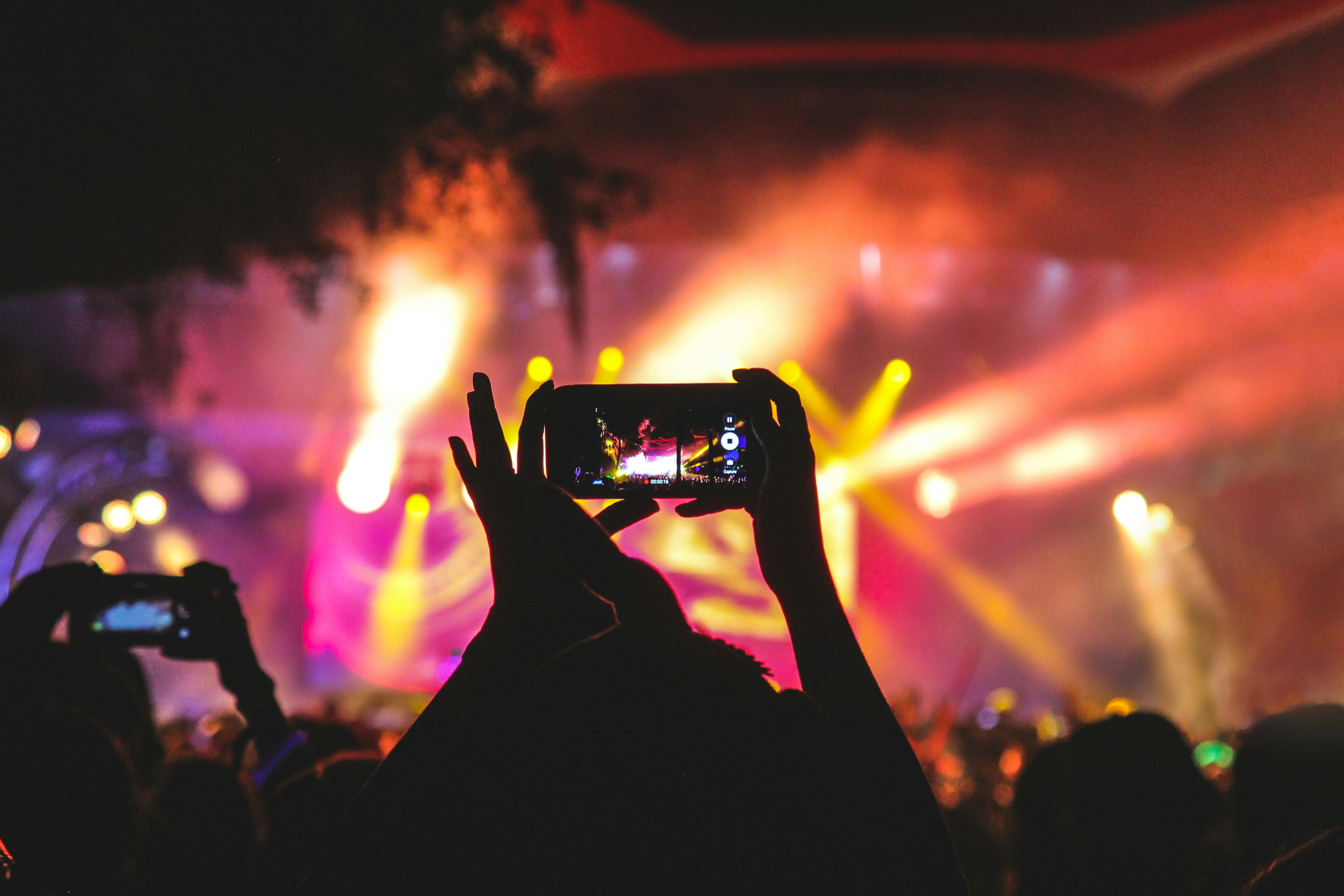 A person holding their phone up to record the stage in a festival crowd 