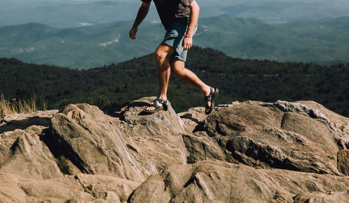 A man wearing his hiking sandals on a rocky landscape