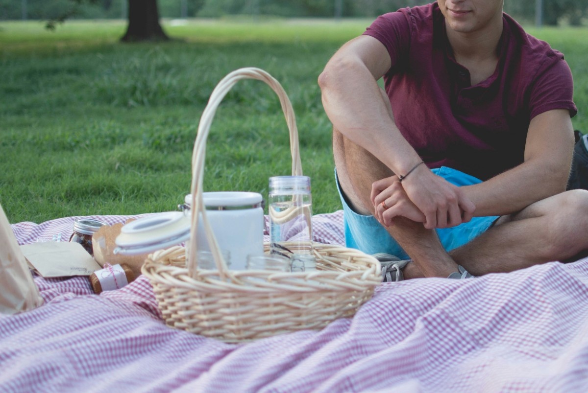 A man sat on a picnic blanket with a picnic basket 