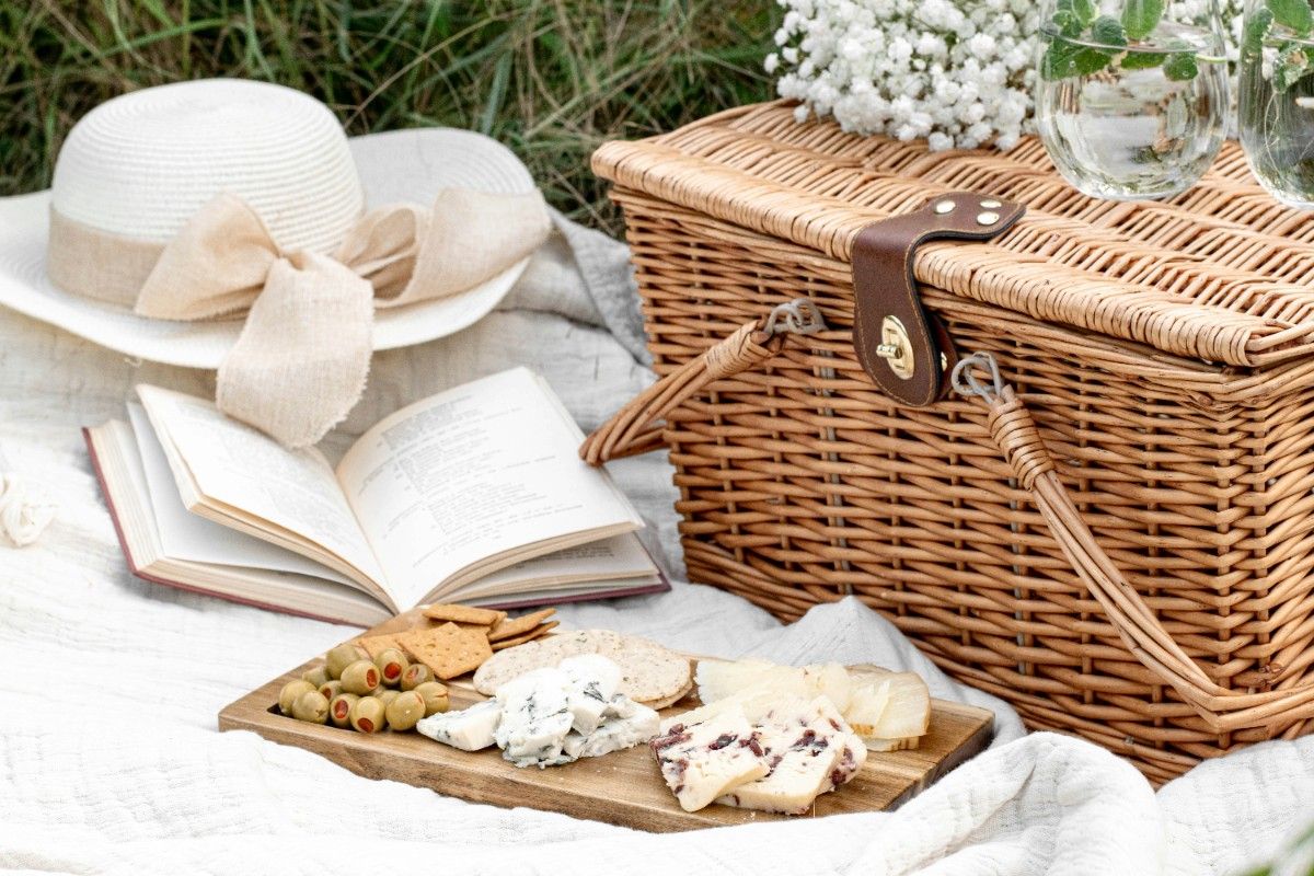 A picnic basket with a cheeseboard in front of it 