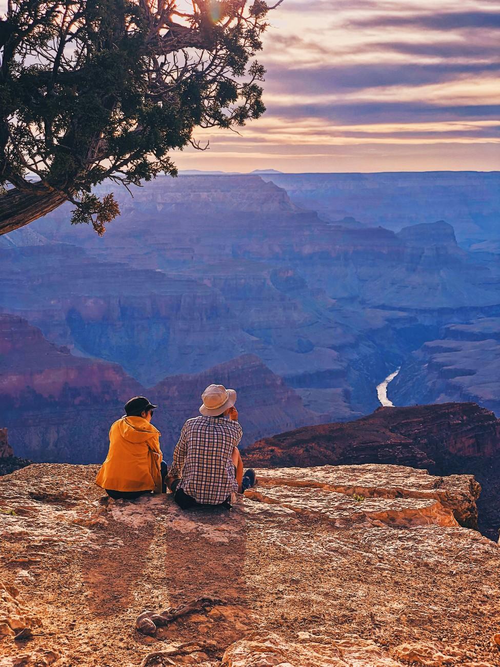 A couple sat on the edge of a rock formation looking out to the Grand Canyon