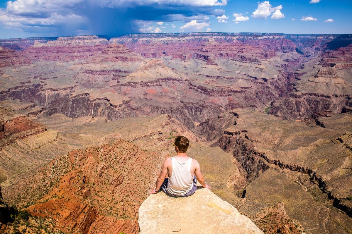 A man sat on the edge of a rock formation looking out to the Grand Canyon