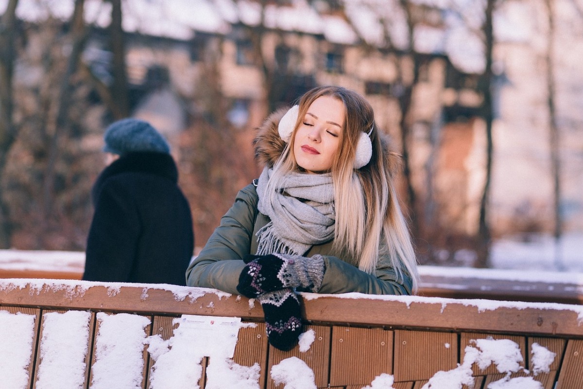 A woman leaning against a wall in the snow wearing mittens 