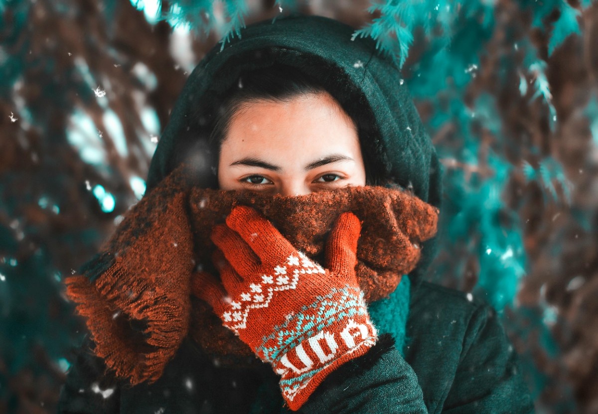 A woman covering her face in her wool gloves in the snow 