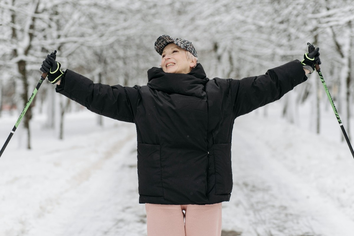 A woman stretching out her arms in her ski gloves, holding ski poles in the snow 