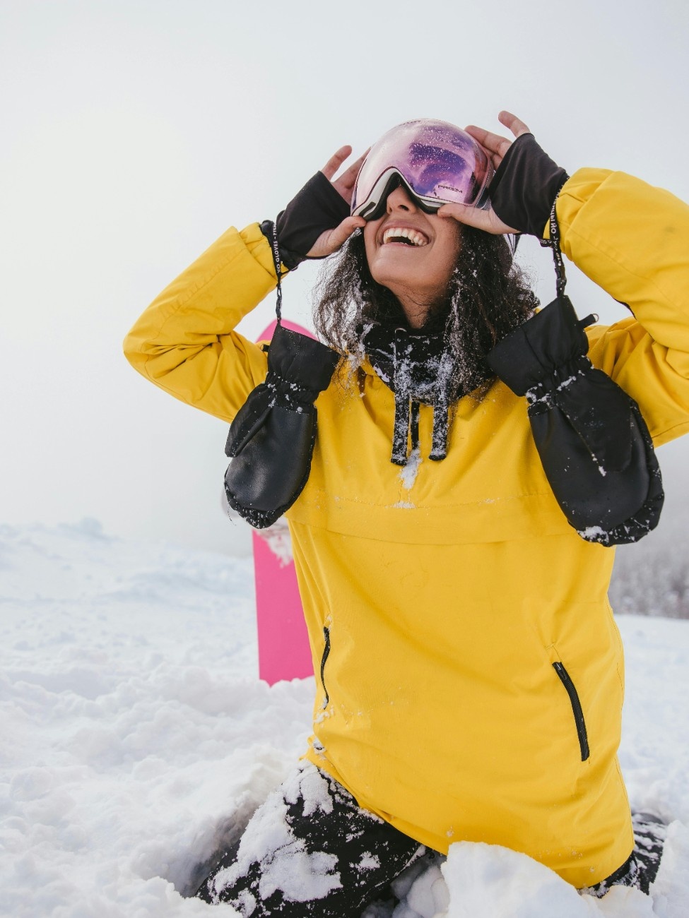 A woman in her snowsports gear, with her ski mittens hanging down 