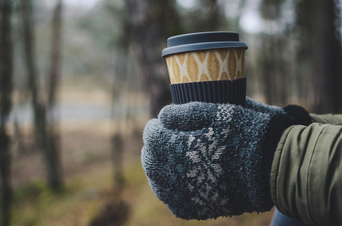 A woman holding a cup of coffee in her mittens 