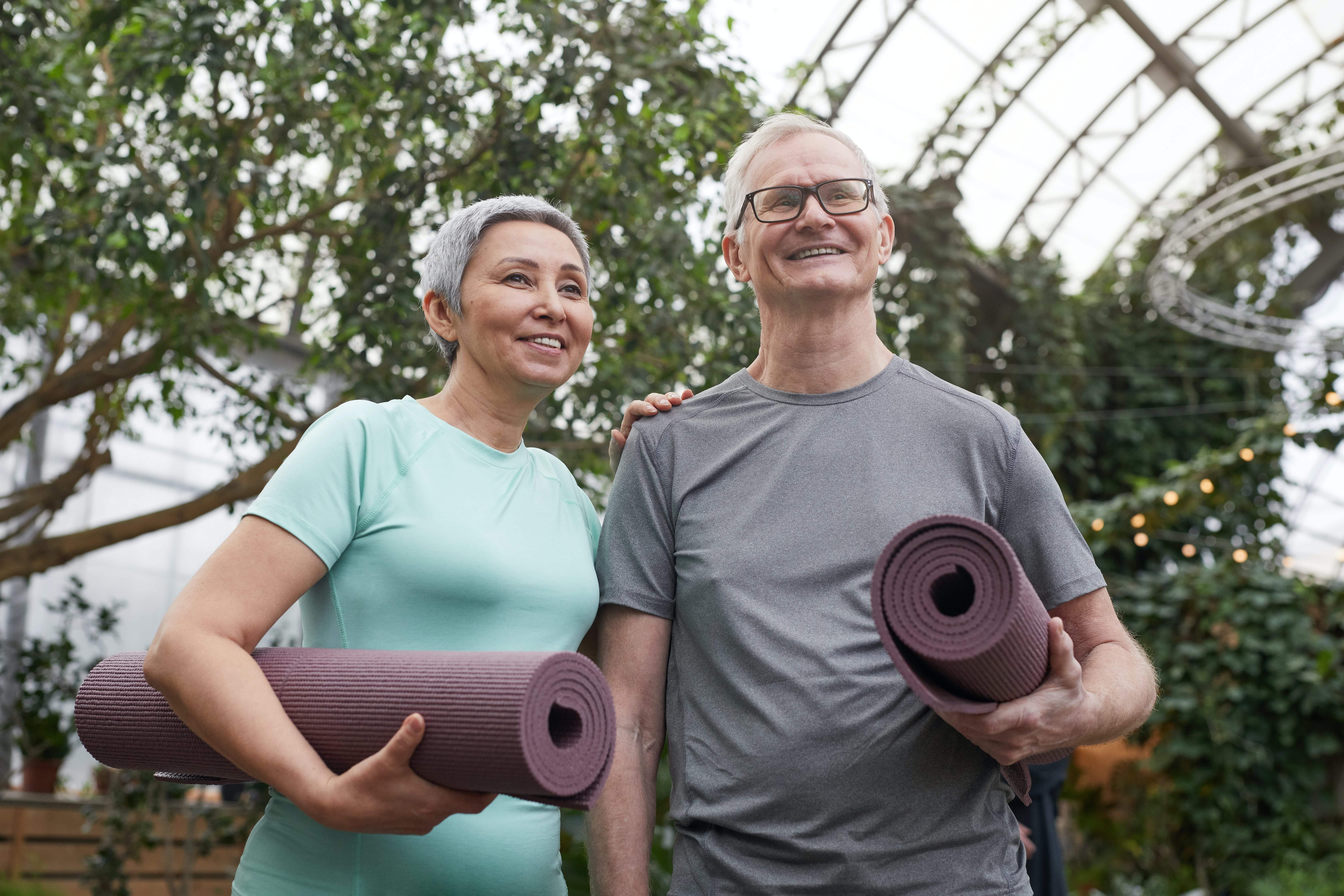 A couple holding their yoga mats, preparing to do a yoga session, smiling 