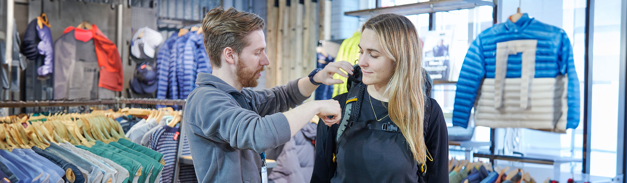 A shop assistant is helping to choose f a rucksack to a woman