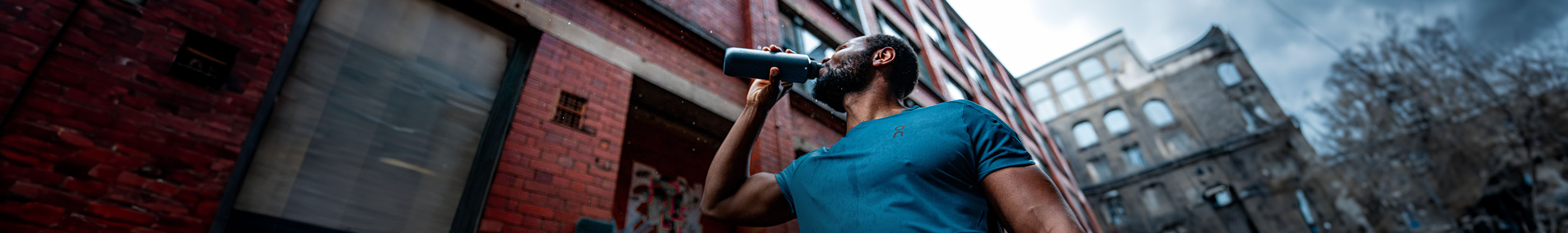 Shop Nutrition & hydration on Runners need. A man in a blue T-shirt drinking from a bottle