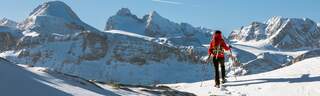 A woman is walking with snow shoes in fluffy powder snow in front of the Dachstein Mountains on a beautiful winterday. The region is famous for hiking, skiing,and climbing all over the year.