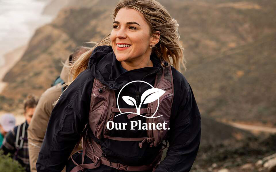 Our Planet range. A woman is smiling and carrying a backpack somewhere outdoors.